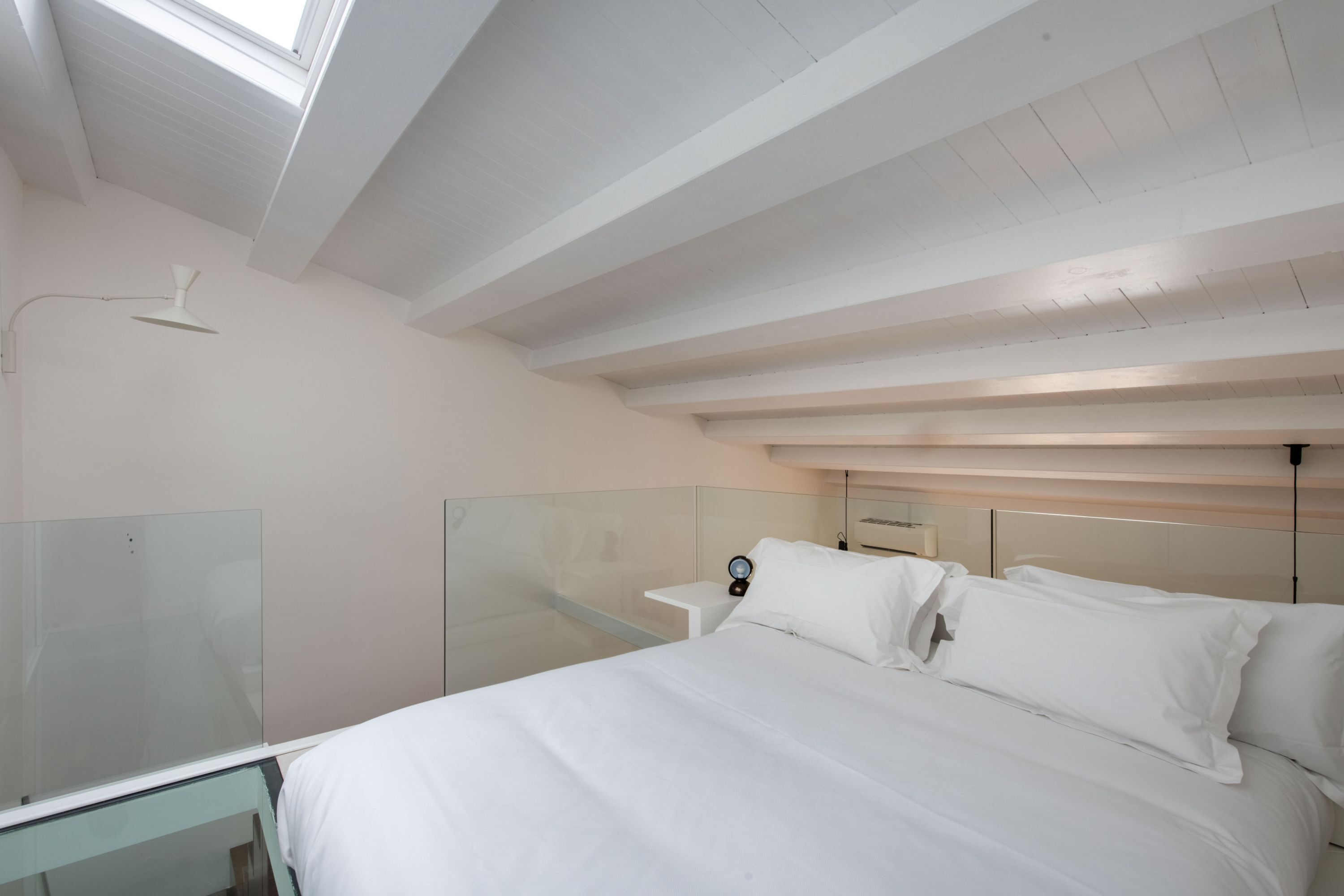 Un dormitorio con cama, mesita de noche y un pequeño espejo.