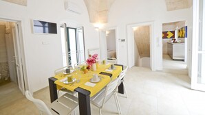 A dining area with a yellow table set for four, white chairs, and a vase with flowers. - Terrazza Isabella by Wonderful Italy (Ostuni)