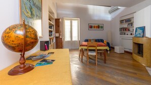 A room with a wooden globe on a table, a dining area with a table and chairs, a bookshelf, and a fireplace.