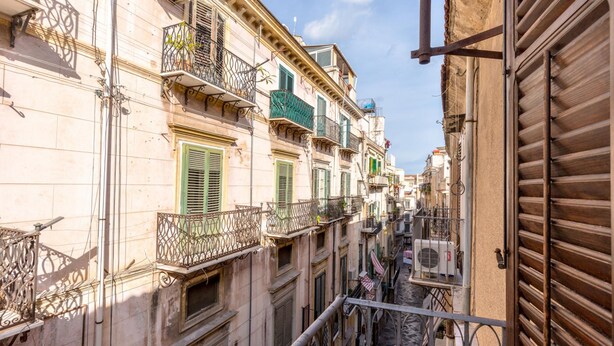 A narrow street with buildings featuring balconies and shutters.