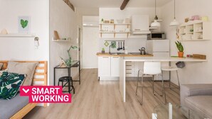 Cocina compacta con armarios blancos, una isla central y un comedor con una mesa y sillas.