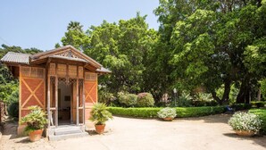 Une structure traditionnelle en bois, ornée de sculptures complexes, entourée d’une végétation luxuriante et de plantes en pot.