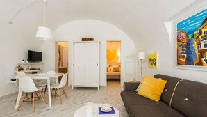 Un salon moderne avec une table à manger blanche, des chaises blanches, une table basse ronde, un canapé marron foncé agrémenté d’un coussin jaune, un meuble blanc et un tableau accroché au mur.