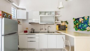 Une cuisine moderne avec des armoires blanches, un réfrigérateur en acier inoxydable, un four à micro-ondes et un évier. On peut voir une chaise et une plante en pot sur le comptoir.