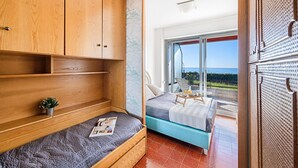 Un dormitorio con un amplio armario de madera, una cama con colchón azul y un balcón con vistas al mar.