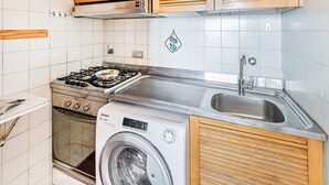 Una cocina compacta con armarios de madera, estufa a gas, lavadora y un lavamanos.