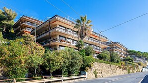 Un edificio residencial de varios pisos con balcones, un muro de contención de piedra y abundante vegetación.