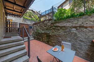 Un patio con una mesa para dos, una botella de vino y un plato de comida.
