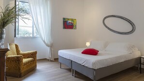 A bedroom with a bed, a chair, a potted plant, a window with curtains, a wall clock, and a framed picture.