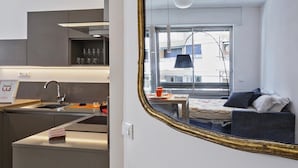 Eine moderne Küche mit Spüle, Arbeitsplatte und einem Spiegel, der einen Wohnbereich mit Sofa und Fenster wiederspiegelt.