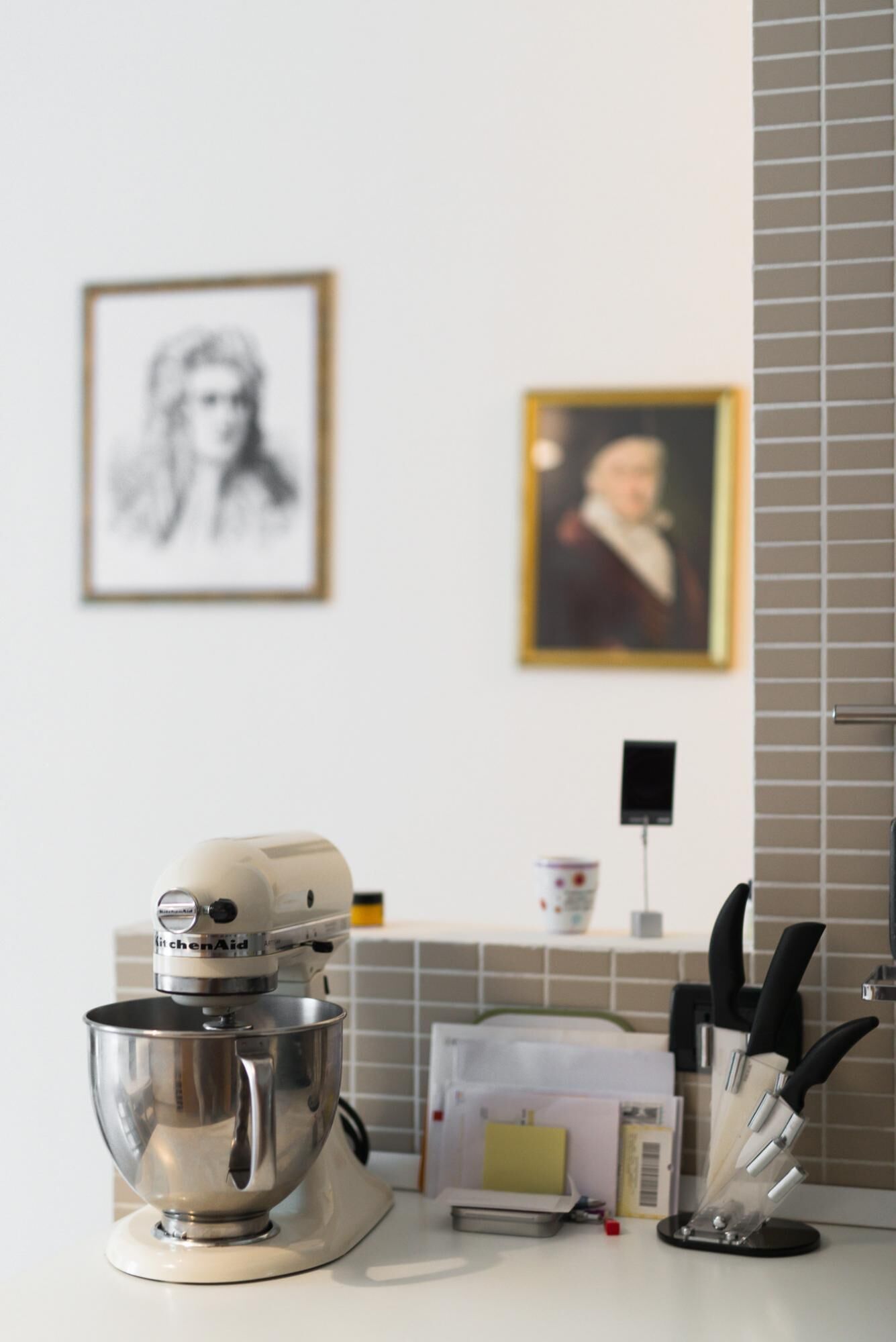 Una encimera de cocina con una batidora de pie, un bloque de cuchillos y dos cuadros en la pared.