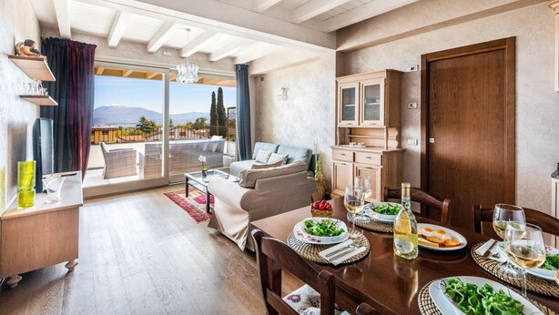 A spacious living area with a dining table set for a meal, a sofa, and a view of the outdoors. - Warda C11 con Piscina by Wonderful Italy (Desenzano del Garda)