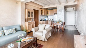 A spacious living area with a sofa, armchair, and dining table. A kitchen with wooden cabinets and appliances is visible in the background. - Warda C11 con Piscina by Wonderful Italy (Desenzano del Garda)