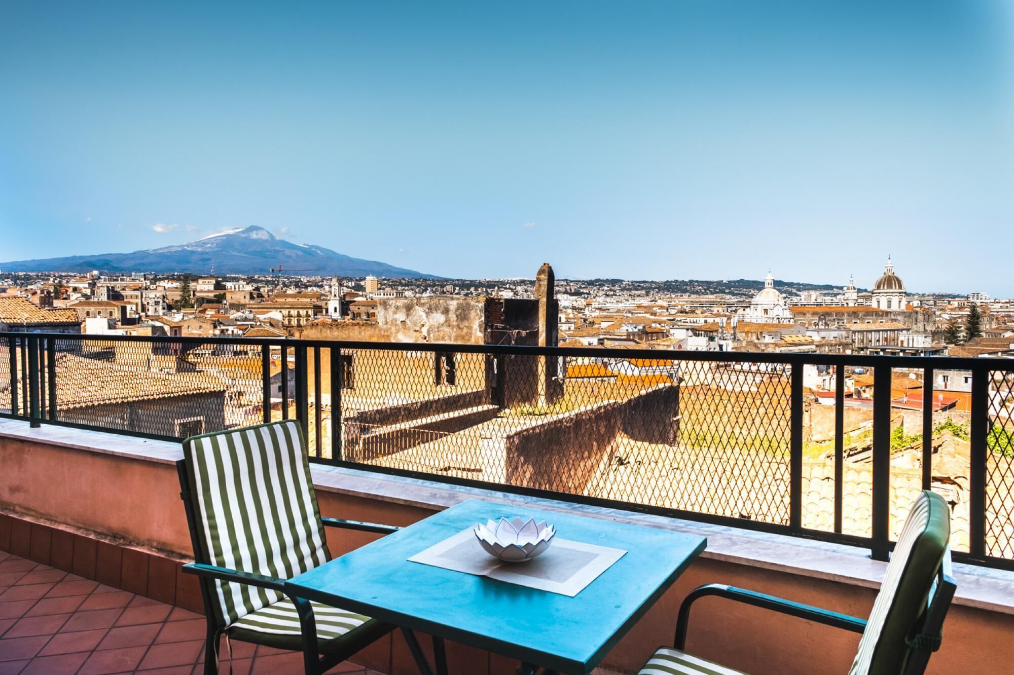 A balcony with a table and chairs, overlooking a cityscape with historic buildings and a mountain in the distance.