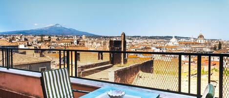 A balcony with a table and chairs, overlooking a cityscape with historic buildings and a mountain in the distance.