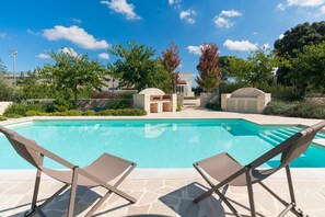 A swimming pool with two lounge chairs, stone walls, and a stone archway.