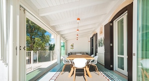 A covered outdoor dining area with a table and chairs, a ceiling with hanging lights, and a view of the outside.