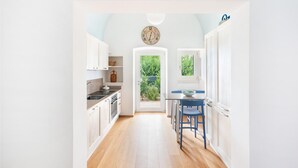 A modern kitchen with white cabinets, a wooden floor, and a view of greenery outside. - Villa Marangi con Piscina (Taurisano)