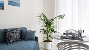 En moderne stue med en blå sofa, en potteplante og et spiseområde med et bord dækket til to personer.