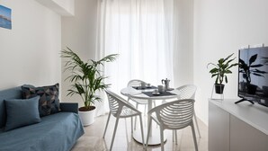 En moderne stue med sofa, spisebord med stole, fjernsyn og potteplanter.