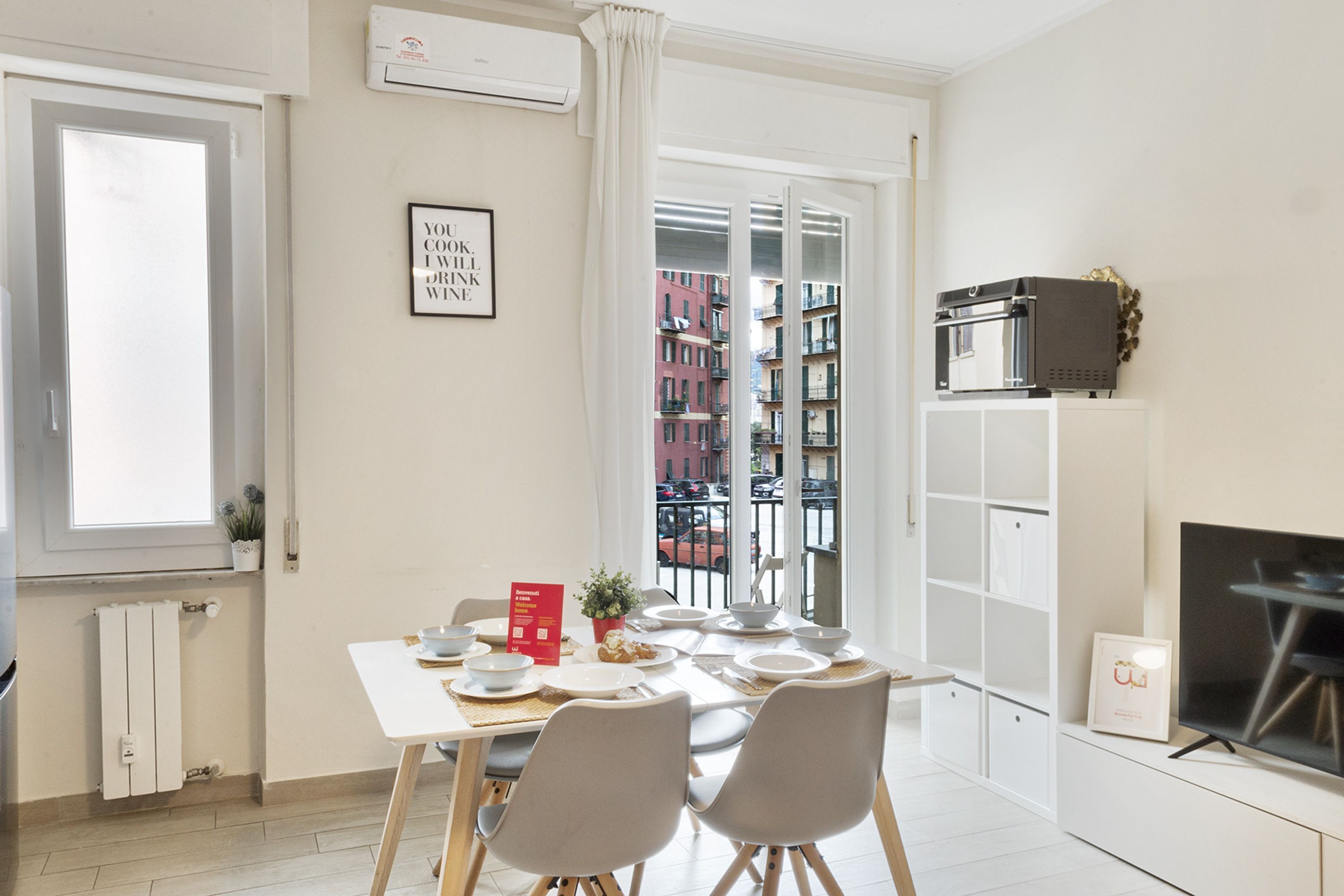 A dining area with a table set for two, a potted plant, and a red welcome sign.