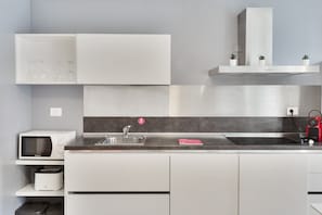 A modern kitchen with white cabinets, a built-in microwave, a sink, and a stainless steel range hood.