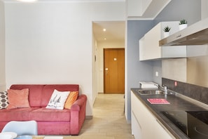 A compact living space with a kitchenette, a red sofa with cushions, and a wooden door in the background. - Corsica Boutique Apartment 10 by Wonderful Italy (Genoa)
