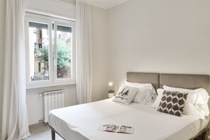 A neatly made bed with a pillow featuring a tree design, a bedside lamp, and a window with white curtains. - Corsica Boutique Apartment 10 by Wonderful Italy (Genoa)