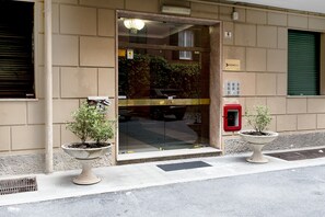 A building entrance with a glass door, two potted plants, a red mailbox, and a travel desk sign.