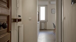 En hall med ett element, en dörr med ett dekorativt handtag, en hylla med diverse föremål och en inramad tavla på väggen.