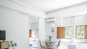 A modern living room with a dining area, large windows with wooden shutters, and a flat-screen TV on a wooden stand. - Euphorbia Apartment by Wonderful Italy (Catania)