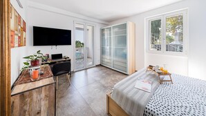 A modern bedroom with a bed, a desk with a laptop, a TV, and a sliding glass door leading to a balcony. - Castelletto 1 - Piscina Jacuzzi by Wonderful Italy (Polpenazze del Garda)