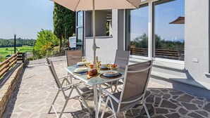 An outdoor dining area with a table set for two, a large umbrella, and a scenic view of a green landscape. - Castelletto 1 - Piscina Jacuzzi by Wonderful Italy (Polpenazze del Garda)