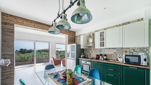 A modern kitchen with green cabinets, a glass dining table, and a view of the outdoors. - Castelletto 1 - Piscina Jacuzzi by Wonderful Italy (Polpenazze del Garda)