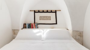 Un dormitorio con una cama blanca, una estantería de madera con libros y un adorno colgante en la pared.