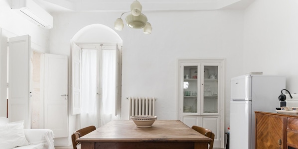 A bright, white room with a wooden dining table, a radiator, a cabinet with glass doors, and a white refrigerator. - Casa Graziella con Terrazza by Wonderful Italy (Ostuni)