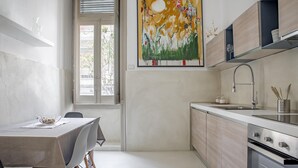 A modern kitchen with a dining area, featuring a large window, a painting, and built-in appliances. - Cavour Apartment Near the Cathedral by Wonderful Italy (Noto)