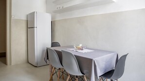 A modern kitchen with a white refrigerator, a dining table with four chairs, and a bowl of fruit on the table. - Cavour Apartment Near the Cathedral by Wonderful Italy (Noto)