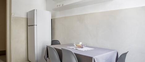 Una cocina moderna con un refrigerador blanco, una mesa de comedor con cuatro sillas y un frutero con fruta en la mesa.