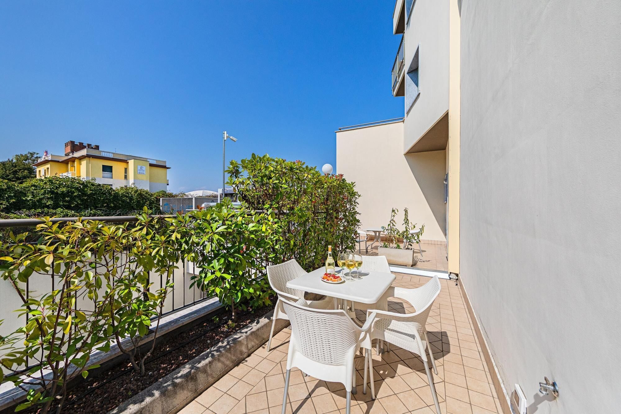 Un balcon avec une table et des chaises, entouré de verdure et surplombant un ciel bleu azur.