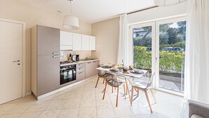 A modern kitchen with a dining area, large windows, and a view of the outdoors.