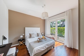 Quarto com uma cama grande, mesa de cabeceira, abajur, bandeja com itens de café da manhã e vista para o verde através de uma porta de vidro deslizante.