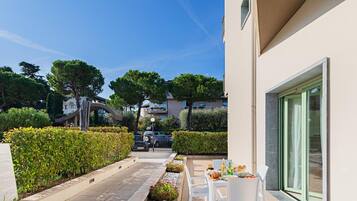 Un'area patio esterna moderna con tavolo e sedie, un vialetto fiancheggiato da piante e vista libera sul quartiere circostante.