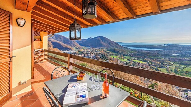 A wooden balcony with a table, chairs, and a bottle of wine. - Poggio sul Clisi 30 Apartment by Wonderful Italy (Villanuova sul Clisi)