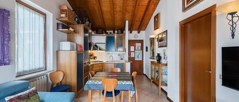 A compact kitchen with wooden beams, a dining table with chairs, a sofa, and a television.