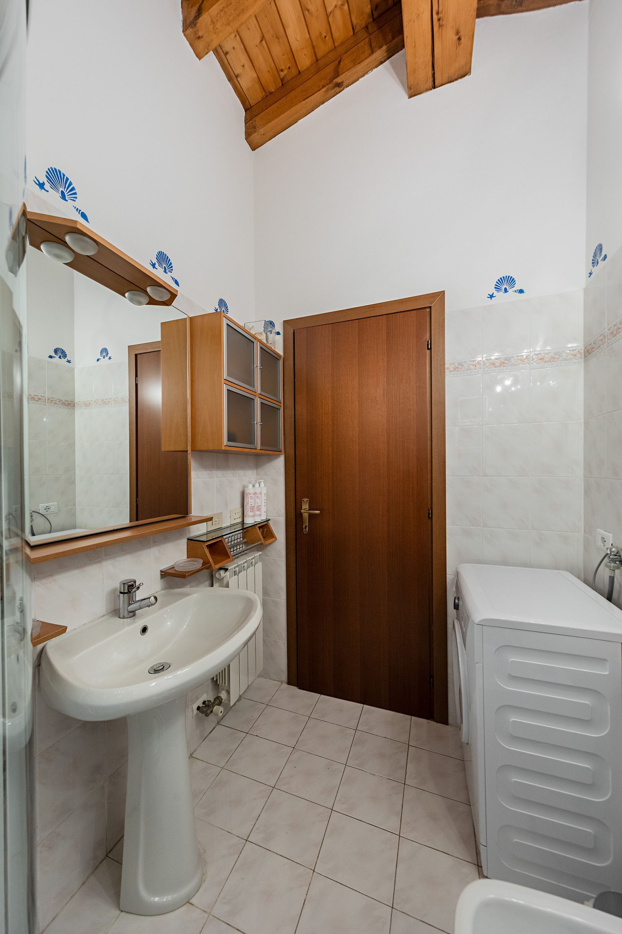 A bathroom with a white sink, wooden cabinets, a mirror, and a wooden door.