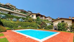 A swimming pool with a red-tiled deck, surrounded by lush greenery and residential buildings. - Poggio sul Clisi 30 Apartment by Wonderful Italy (Villanuova sul Clisi)
