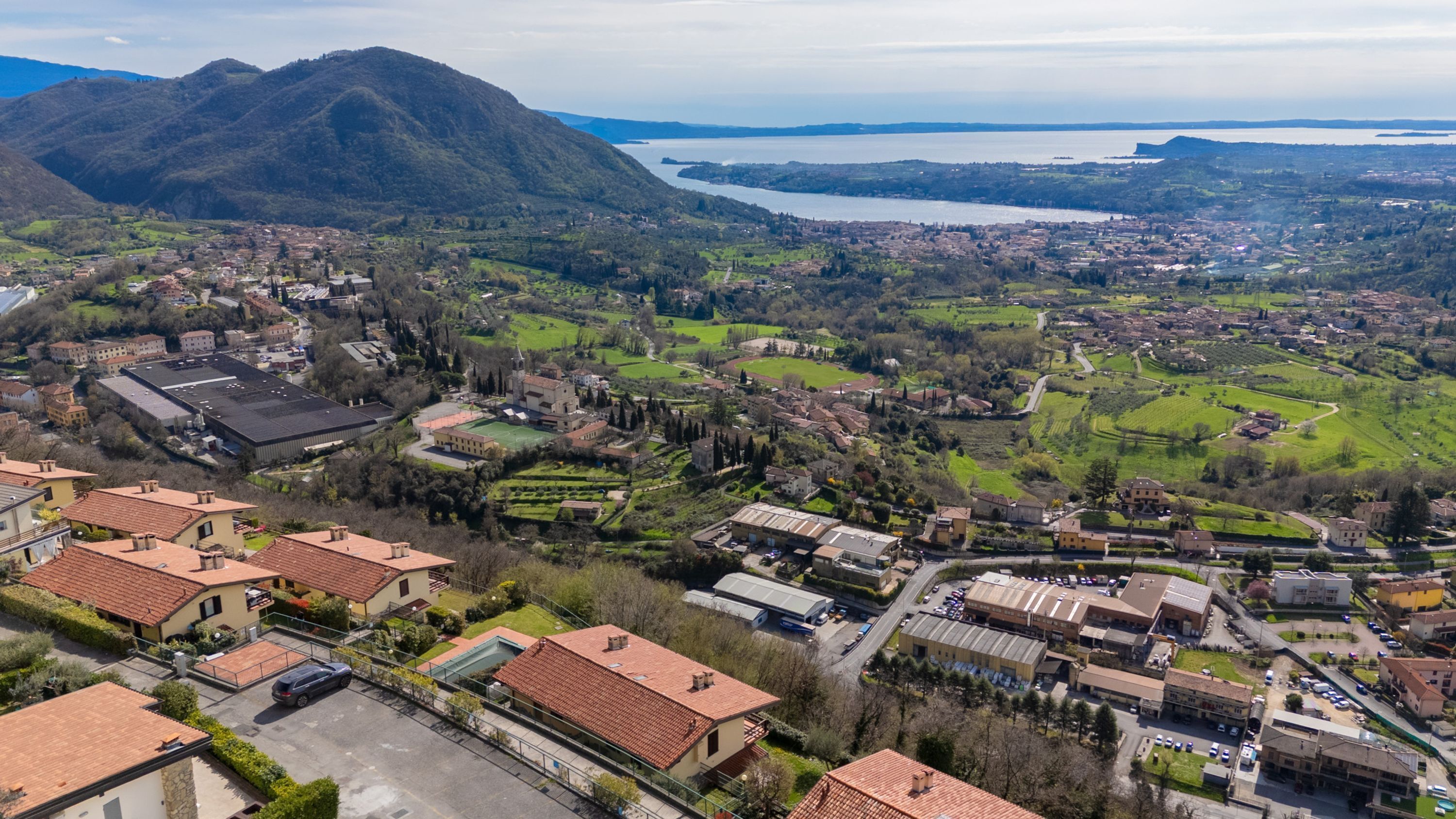 An aerial view of a town with residential buildings, green fields, and a mountain in the background.
