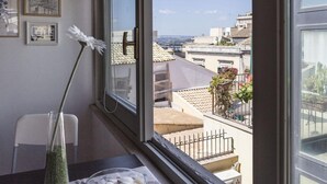 A room with a large window overlooking a cityscape, a vase with a single flower, and a bowl of seashells on a table. - Salomone Apartment 13 With Terrace by Wonderful Italy (Syracuse)