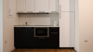 A compact kitchen with white upper cabinets, a black lower cabinet, a built-in microwave, and a white refrigerator. - Il Loggiato - Stella Apartment by Wonderful Italy (Naples)